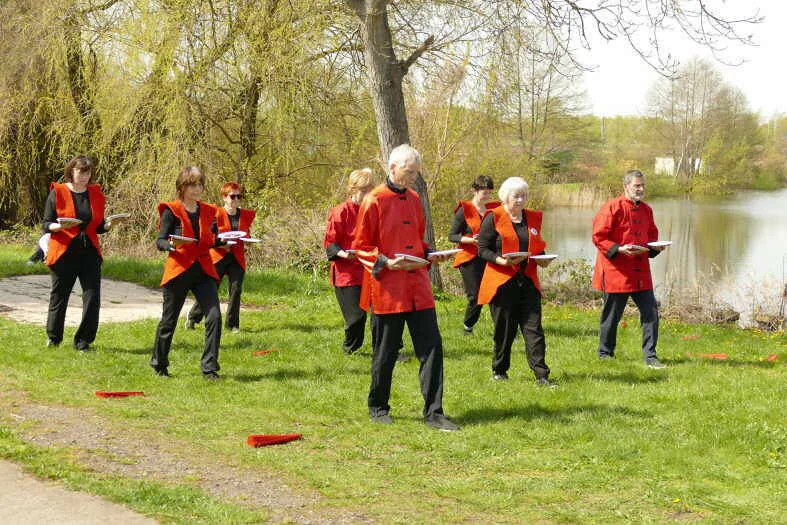 Qi-Gong-Gruppe bei einer Tellerübung auf einer Wiese am Wasser