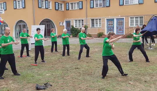 Gruppe in grünen Shirts bei Tai-Chi-Stockübungen im Freien